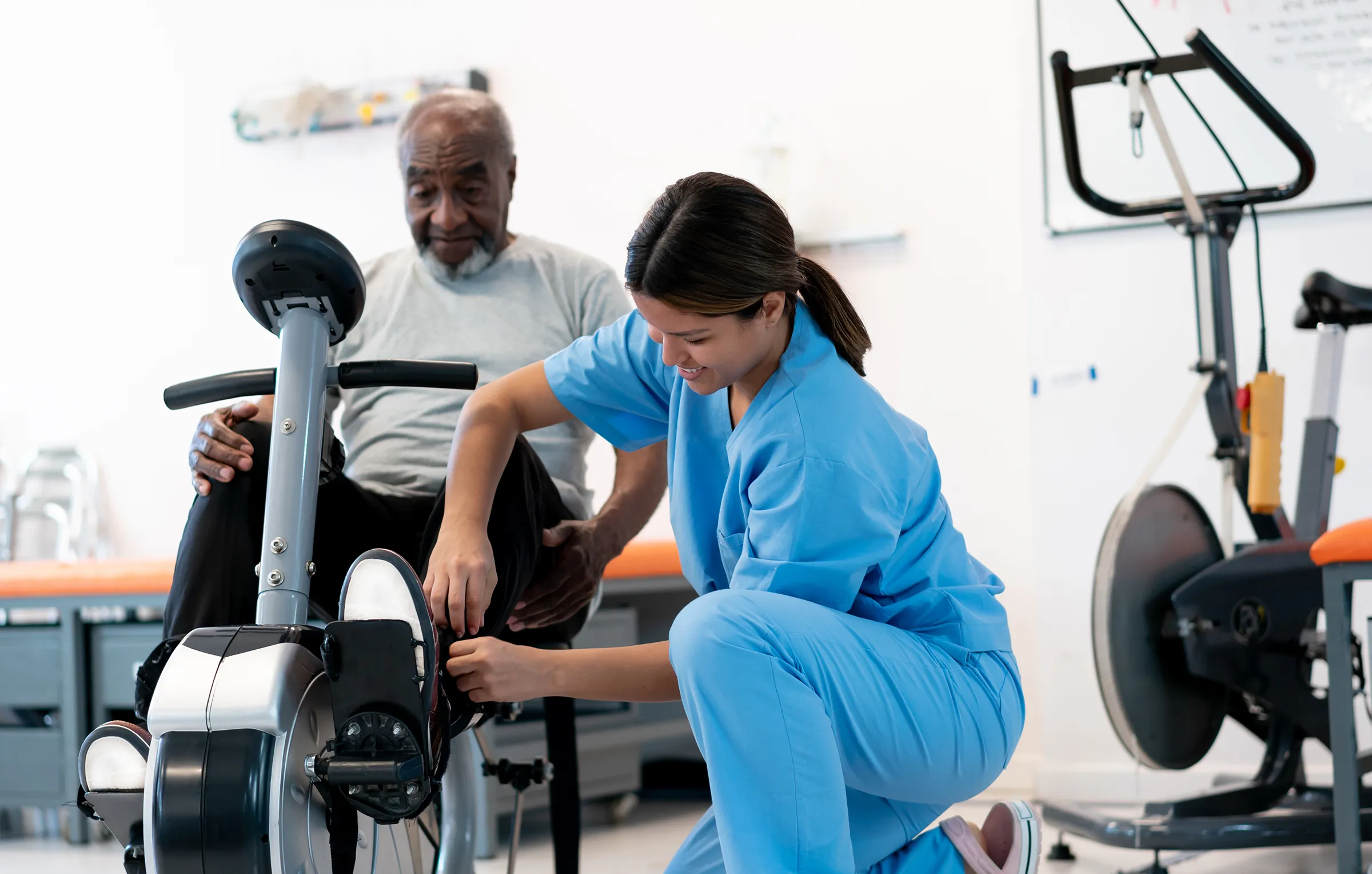 Physical therapist assisting senior man on exercise bike