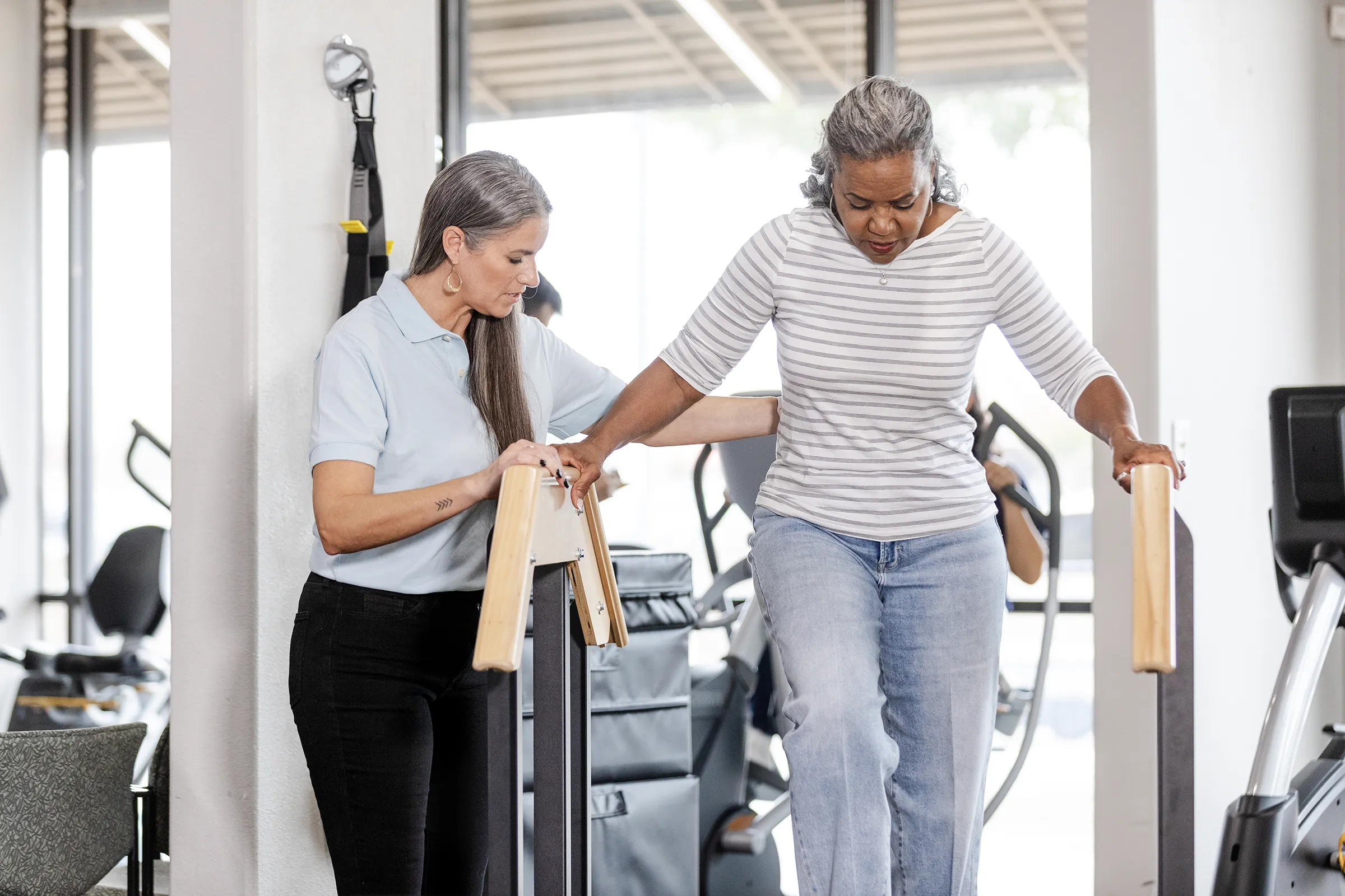 Physical therapist assisting woman with parallel bar walking