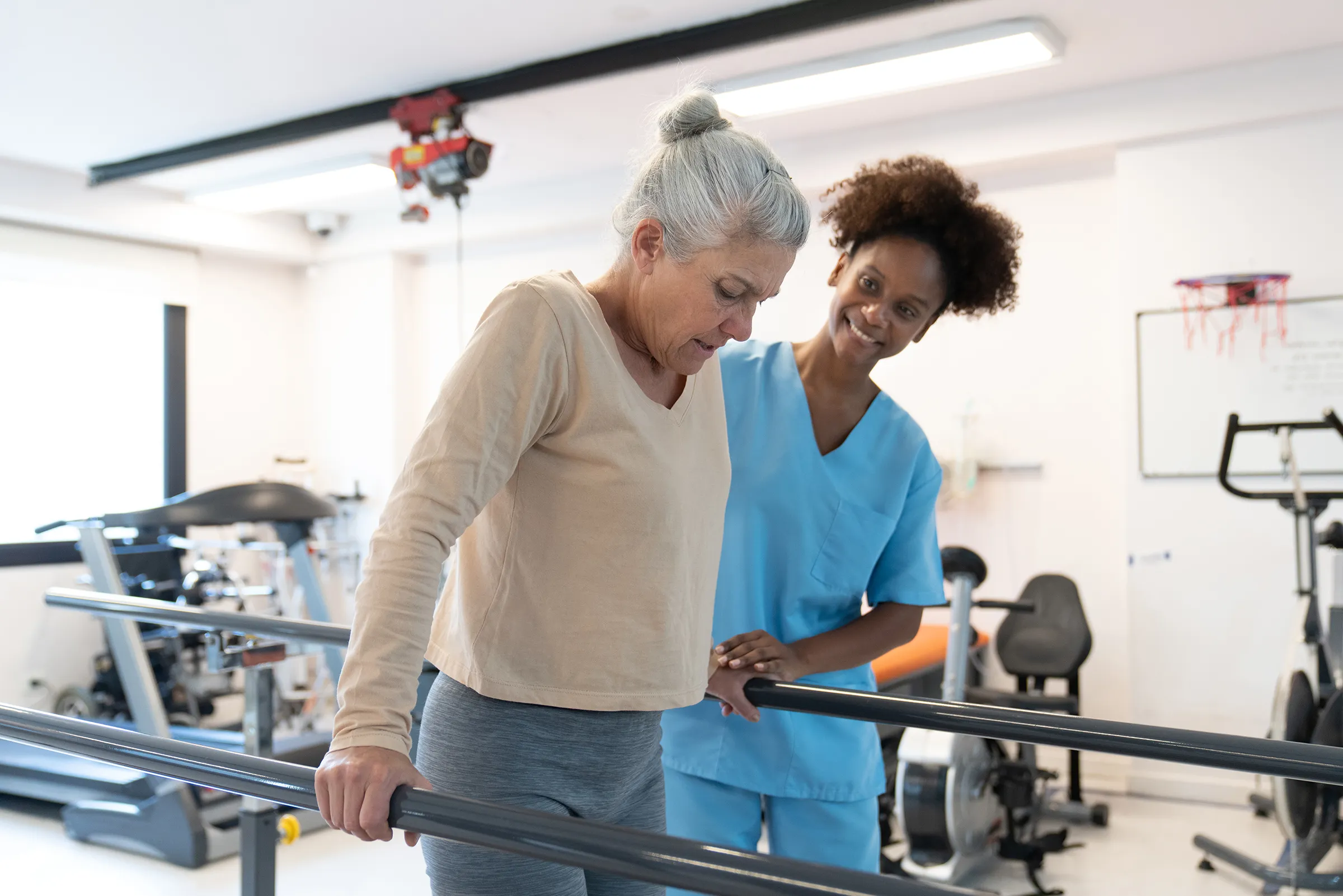 Physical therapist assisting senior woman with parallel bars