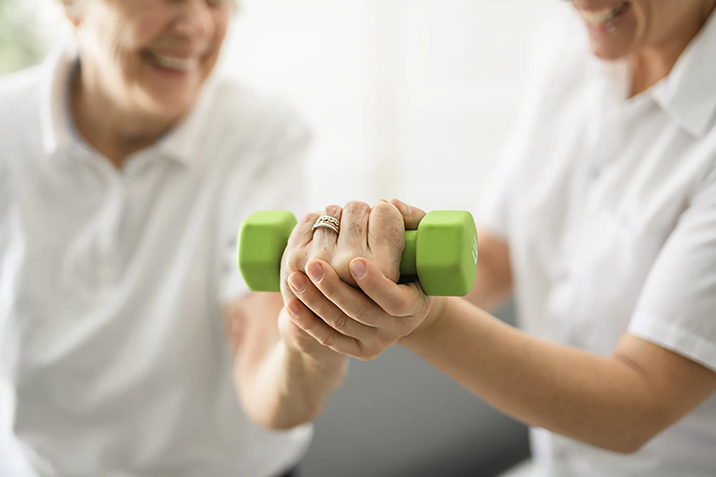 Senior lifting green dumbbell with caregiver assistance