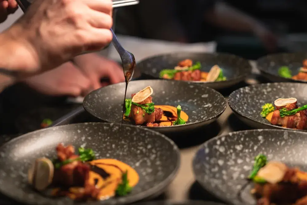 Chef drizzling sauce over gourmet plated dishes