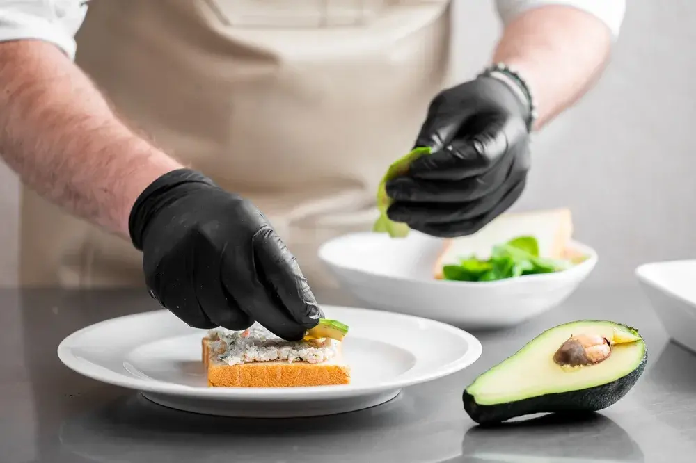 Chef garnishes open-faced sandwich beside halved avocado