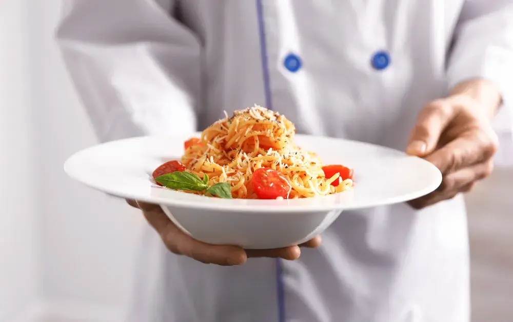 Chef holding pasta with tomatoes, basil, and grated cheese